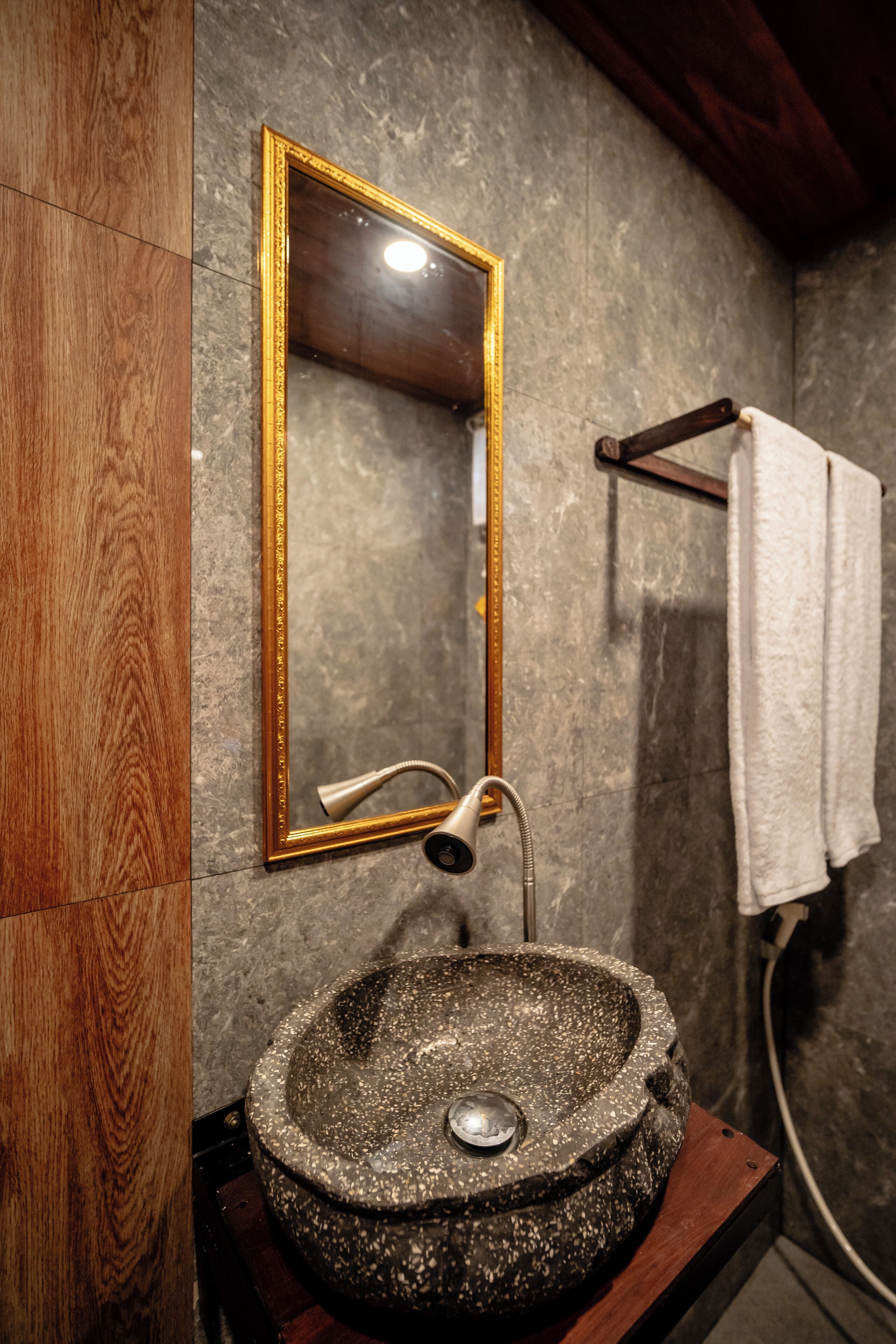 A bathroom with a stone sink, wooden vanity, a gold-framed mirror, and a towel rack.