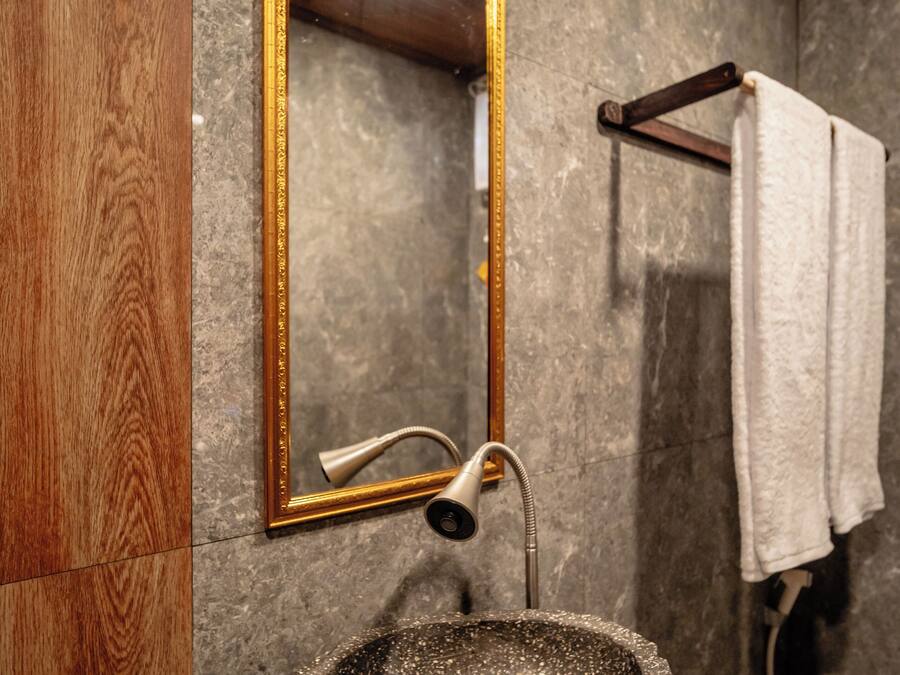 A bathroom with a stone sink, wooden vanity, a gold-framed mirror, and a towel rack.