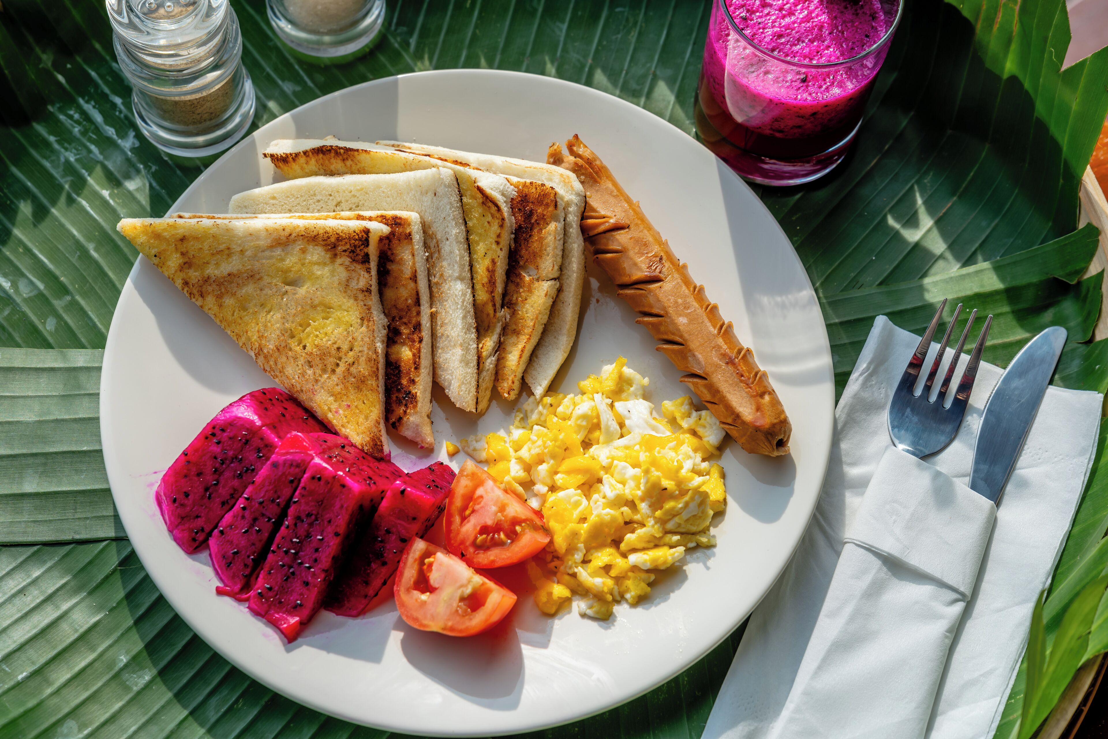 A plate with toast, scrambled eggs, a fried egg, dragon fruit, and tomato slices.