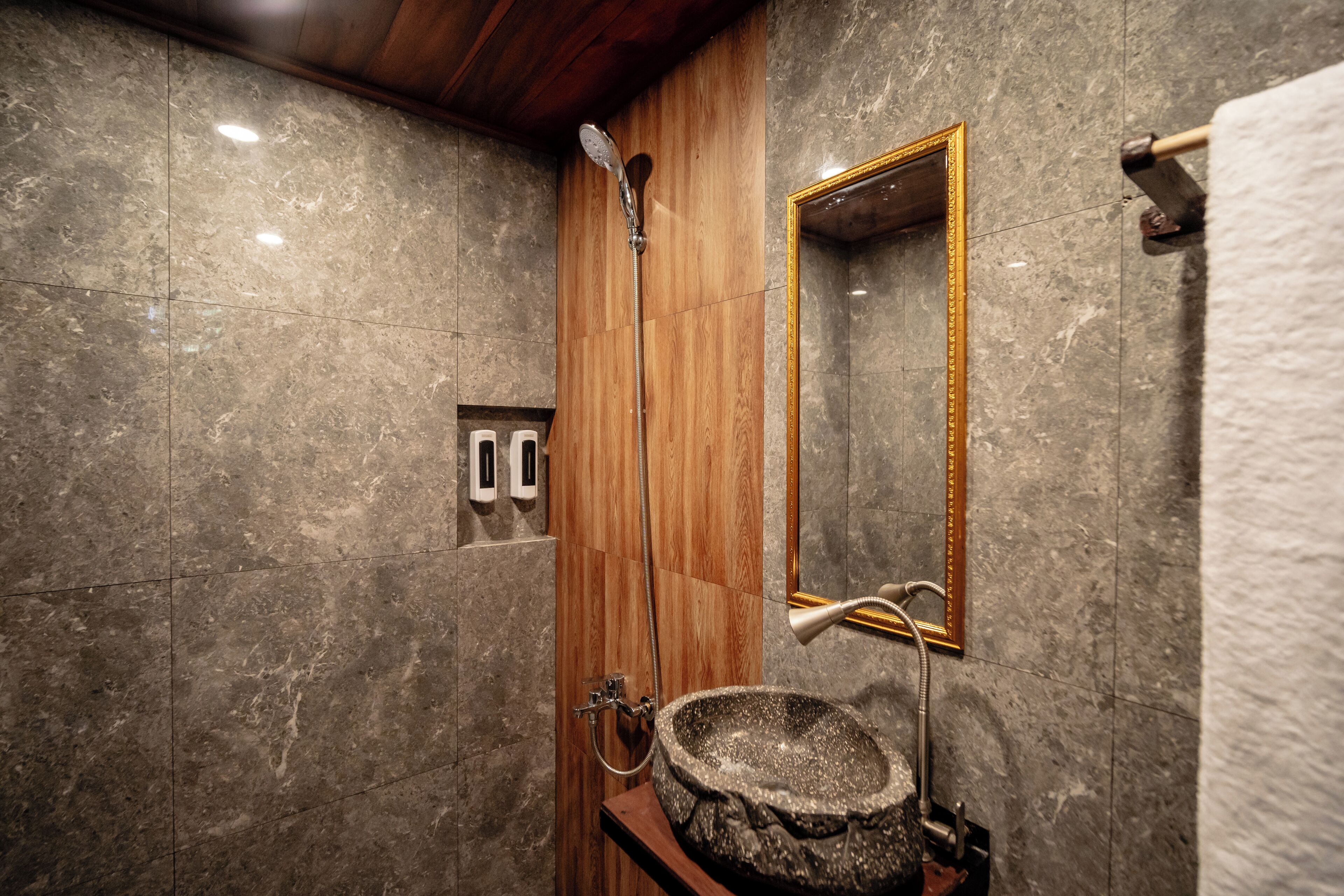A bathroom with a stone sink, wooden shower enclosure, and a mirror with a gold frame.