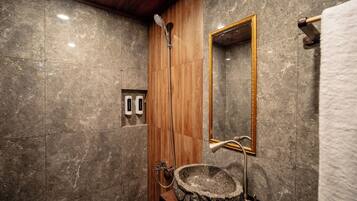 A bathroom with a stone sink, wooden shower enclosure, and a mirror with a gold frame.