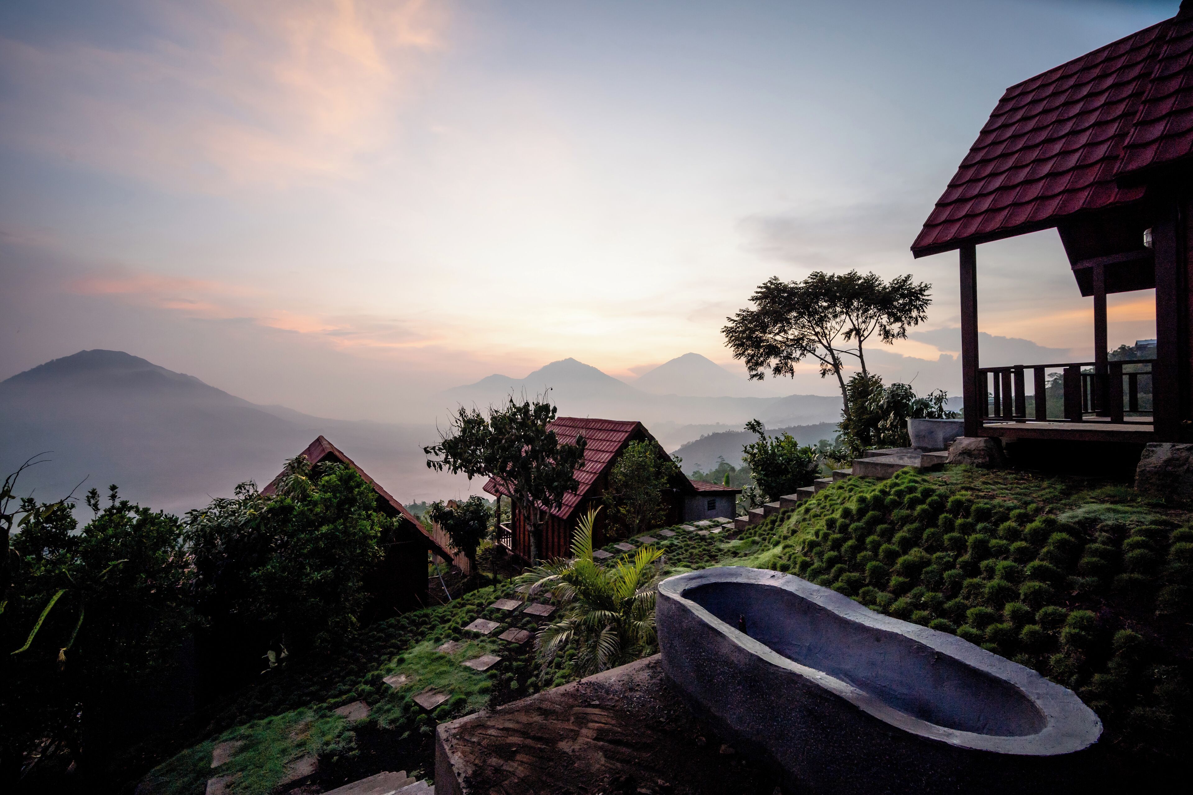 A serene landscape with a stone bathtub, a wooden structure with a red roof, and a lush garden.