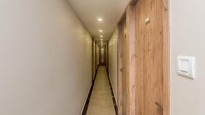 Un pasillo estrecho y bien iluminado, con puertas de madera a un lado y un interruptor de luz en la pared.