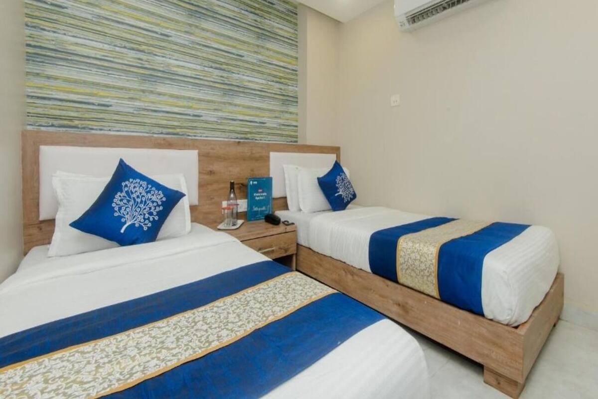 A hotel room with two beds, each with a blue and white bedspread, a wooden headboard, and a wall-mounted air conditioner.