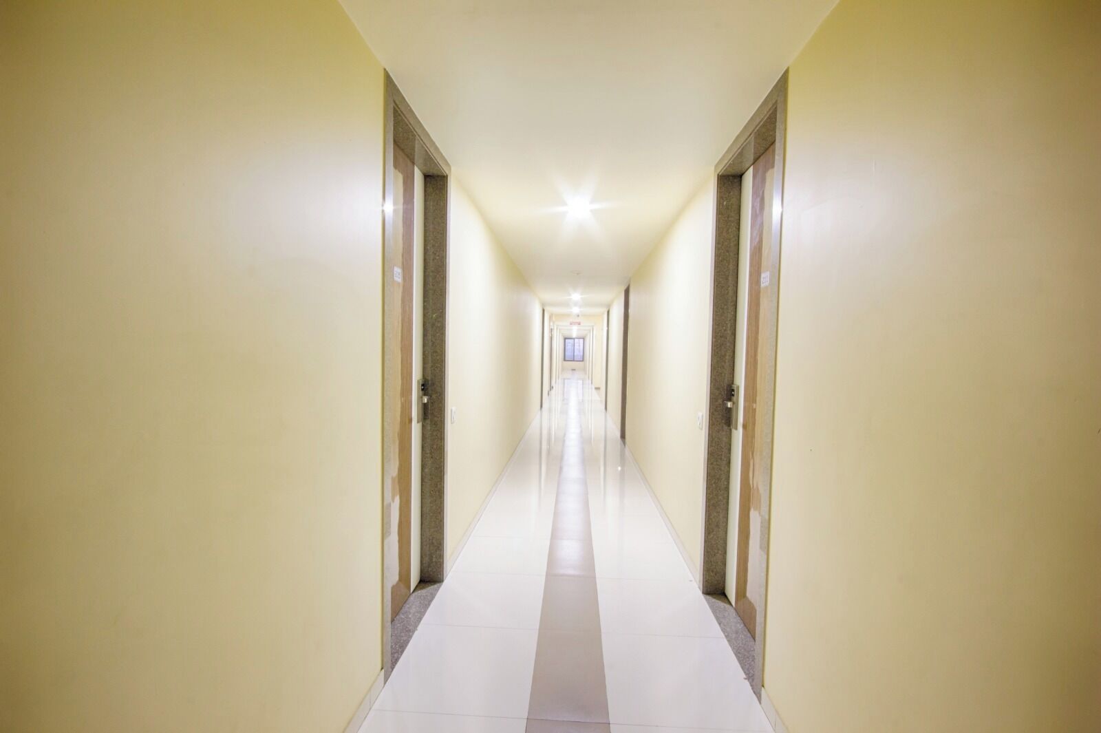 A long, narrow hotel corridor with doors on both sides and a tiled floor.