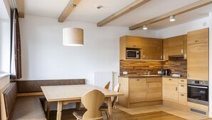 Una cucina moderna con mobili in legno, un forno a microonde integrato e un forno. C'è un tavolo da pranzo in legno con sedie e una panca.