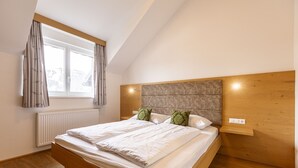 Una camera da letto con un letto in legno, biancheria da letto bianca, una testiera con illuminazione integrata, una finestra con tende e un pavimento in legno.