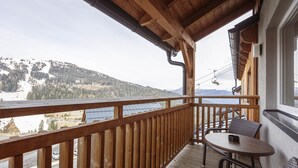 Un balcone in legno con tavolo e sedie, affacciato su un paesaggio montuoso e un corpo d'acqua.