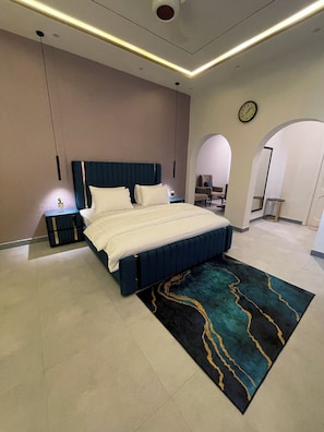 A modern bedroom with a large bed, a bedside table with a lamp, a clock on the wall, and an arched doorway leading to another room. - Loft BnB F10 Guest House (Islamabad)