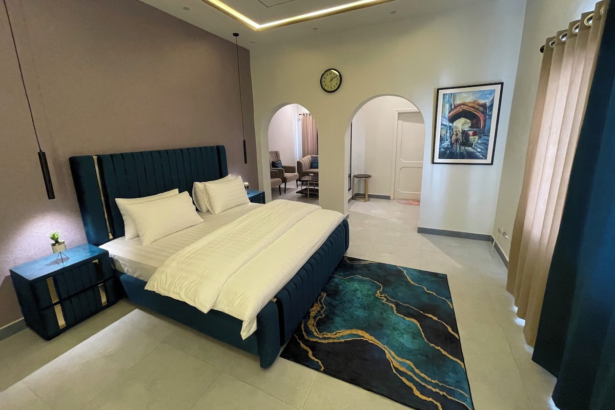 Une chambre à coucher moderne avec un grand lit, des tables de chevet, un tapis et un tableau au mur.