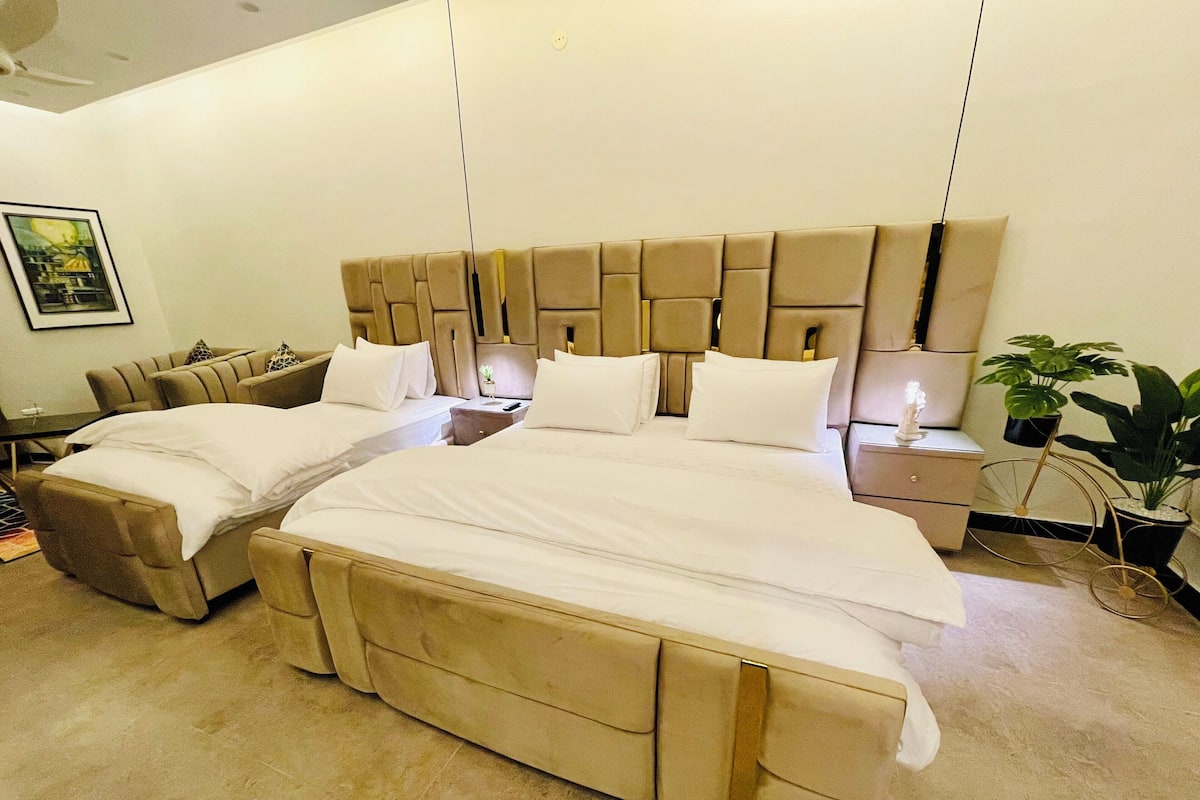 Une chambre d’hôtel avec un grand lit, un lit plus petit, un canapé, une table de chevet et une plante en pot.