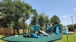 A playground with slides and climbing structures, surrounded by a fenced area and trees. - * Majestic Sun A204 | Gulf Views | Heated Pools * (Miramar Beach)