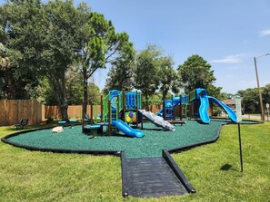 A playground with slides and climbing structures, surrounded by a fenced area and trees. - * Majestic Sun A204 | Gulf Views | Heated Pools * (Miramar Beach)