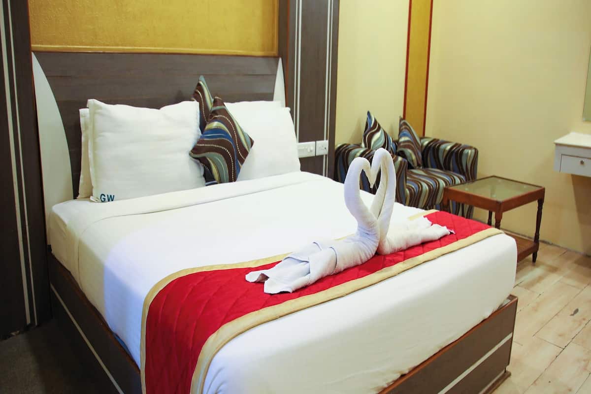 A neatly made bed with a red blanket, white pillows, and a towel arranged in a heart shape.