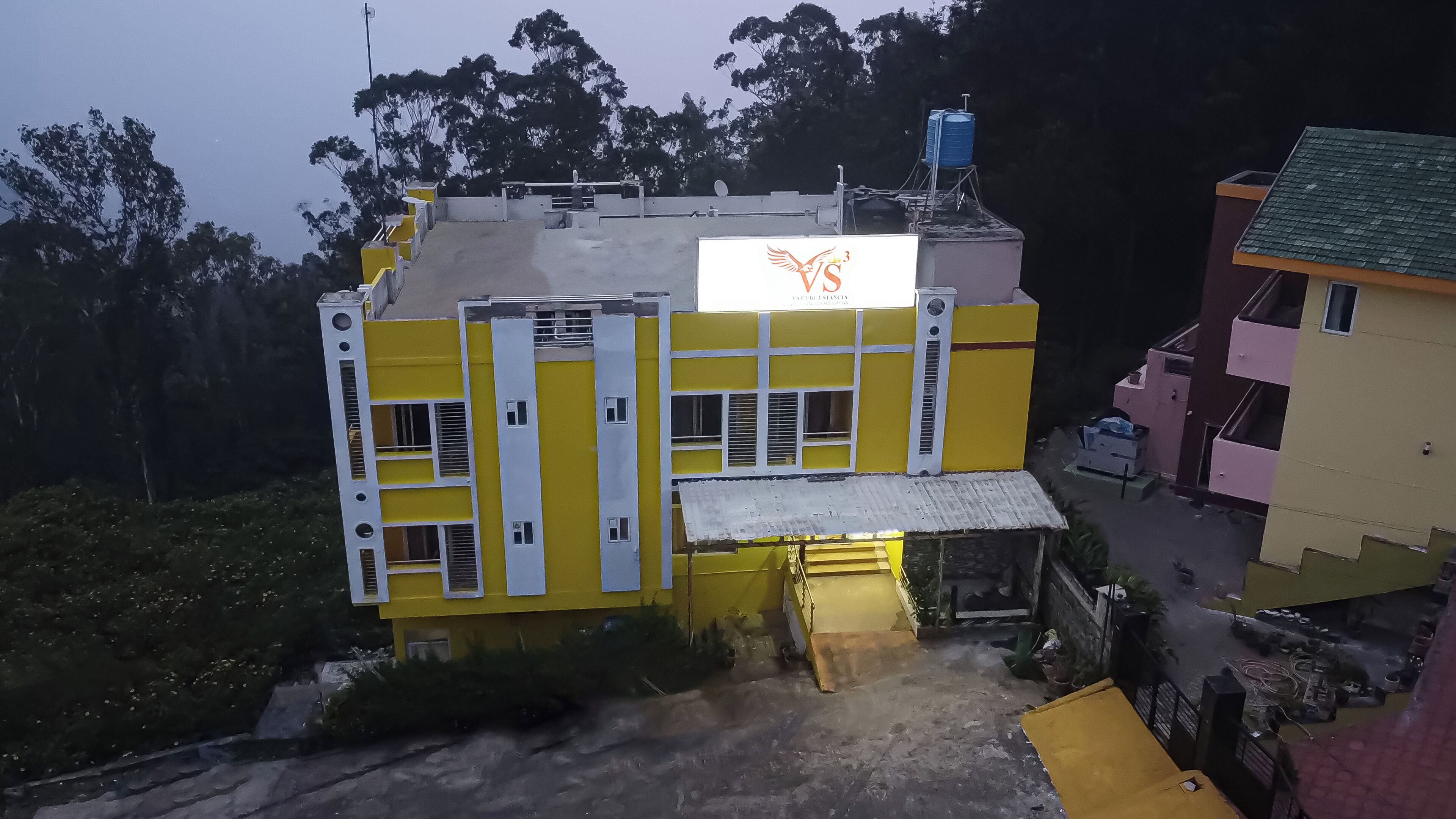 A yellow building with a large sign, a water tank on the roof, and a small structure with a roof.
