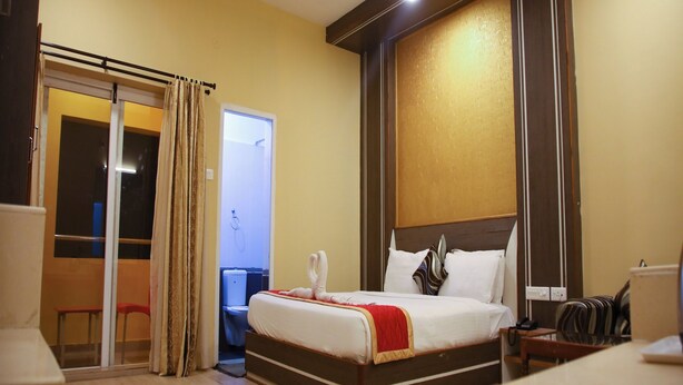 A hotel room with a bed, a desk, a chair, a ceiling fan, and a sliding door leading to a balcony. - VS Cube Estancia (Yercaud)