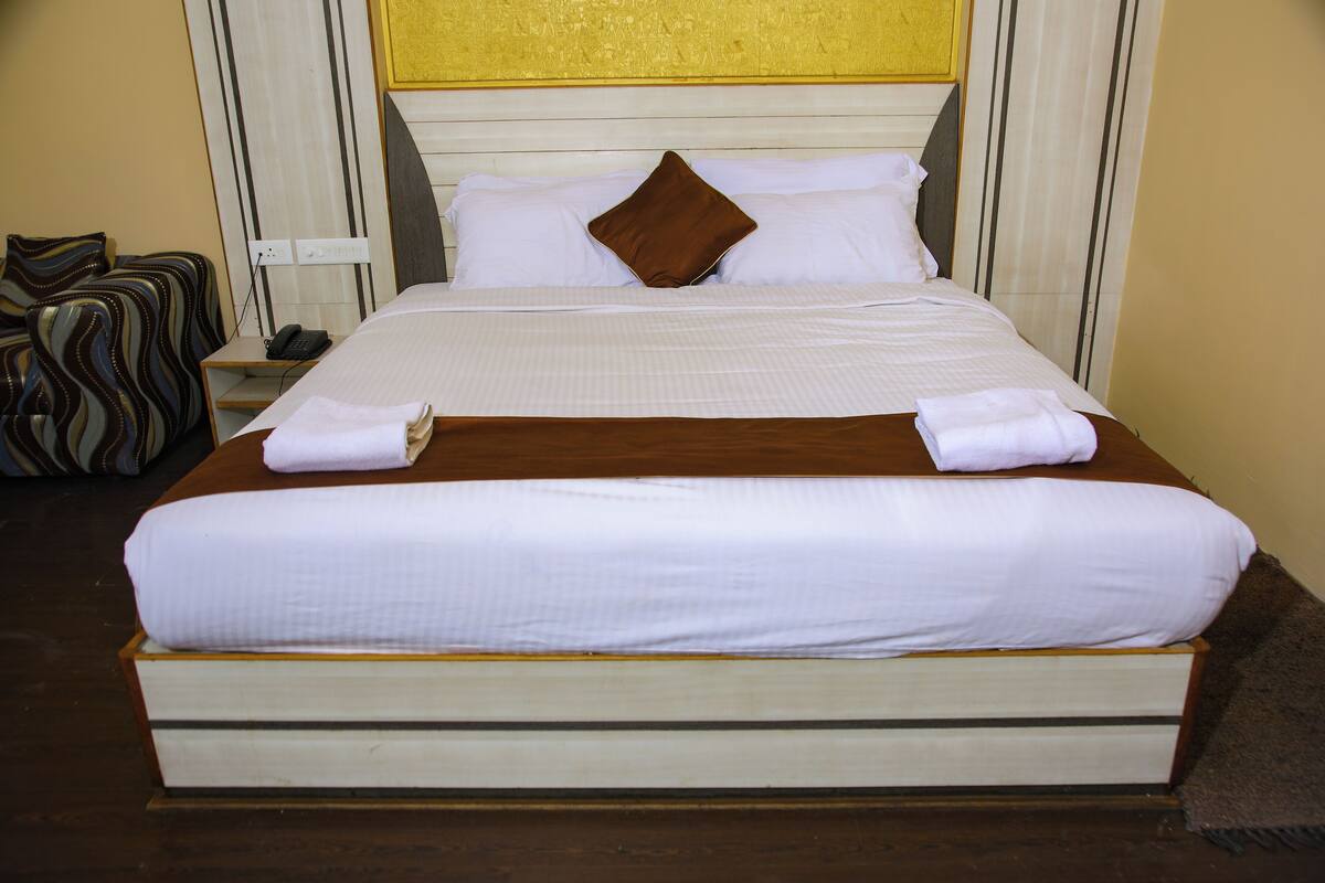 A neatly made bed with white linens and a brown accent pillow, a bedside table with a phone, and a striped chair in a hotel room.