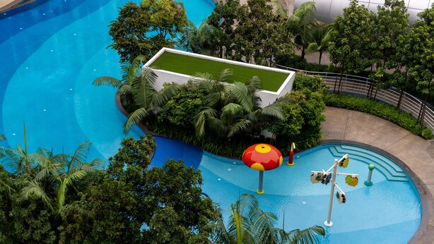 A swimming pool with a green deck area, surrounded by lush tropical vegetation. - Maya Bay Residences (Banting)