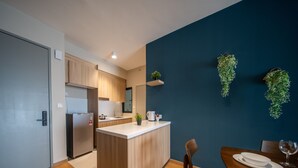 A modern kitchen with wooden cabinets, a built-in island, and a dark blue accent wall with hanging greenery. - Maya Bay Residences (Banting)