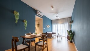 A modern living room with a dining area, featuring a blue wall, wooden furniture, and a ceiling fan. - Maya Bay Residences (Banting)