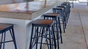 Eine Barbereich mit einem Strohdach, einer Beton-Bar und schwarzen Barhocker.