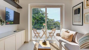 A modern living room with a sofa, coffee table, and TV. There is a balcony with a table and chairs. - El Tigre Luxe & Cozy Stay: Pool, Balcony and WiFi! (Nuevo Vallarta)