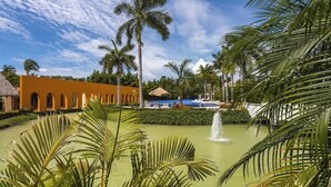 A resort with a pool, palm trees, and a building with arches. - El Tigre Luxe & Cozy Stay: Pool, Balcony and WiFi! (Nuevo Vallarta)