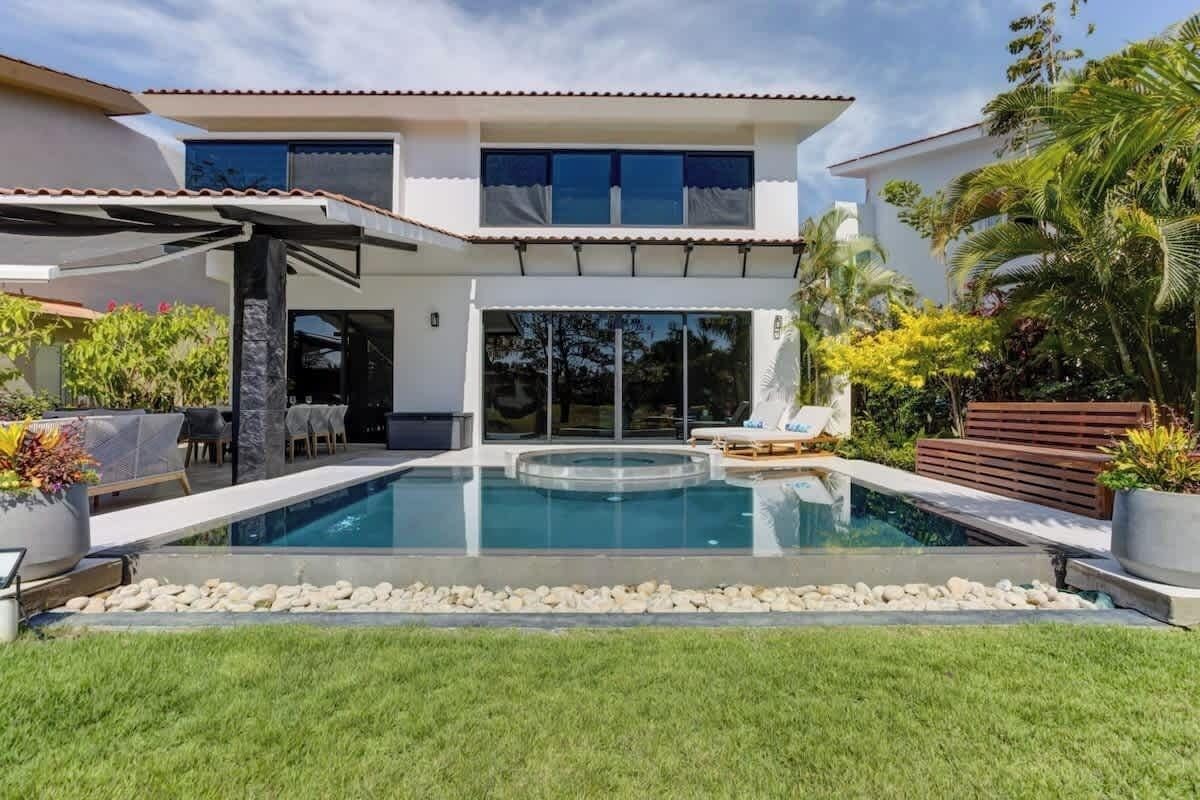 Ein modernes, zweistöckiges Haus mit Swimmingpool, Sitzgelegenheiten im Freien und tropischer Bepflanzung.