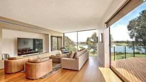 A modern living room with a large flat-screen TV, a sofa, and a coffee table. - Front Row Golf & Lake Views Luxe Coastal Retreat (Torquay)