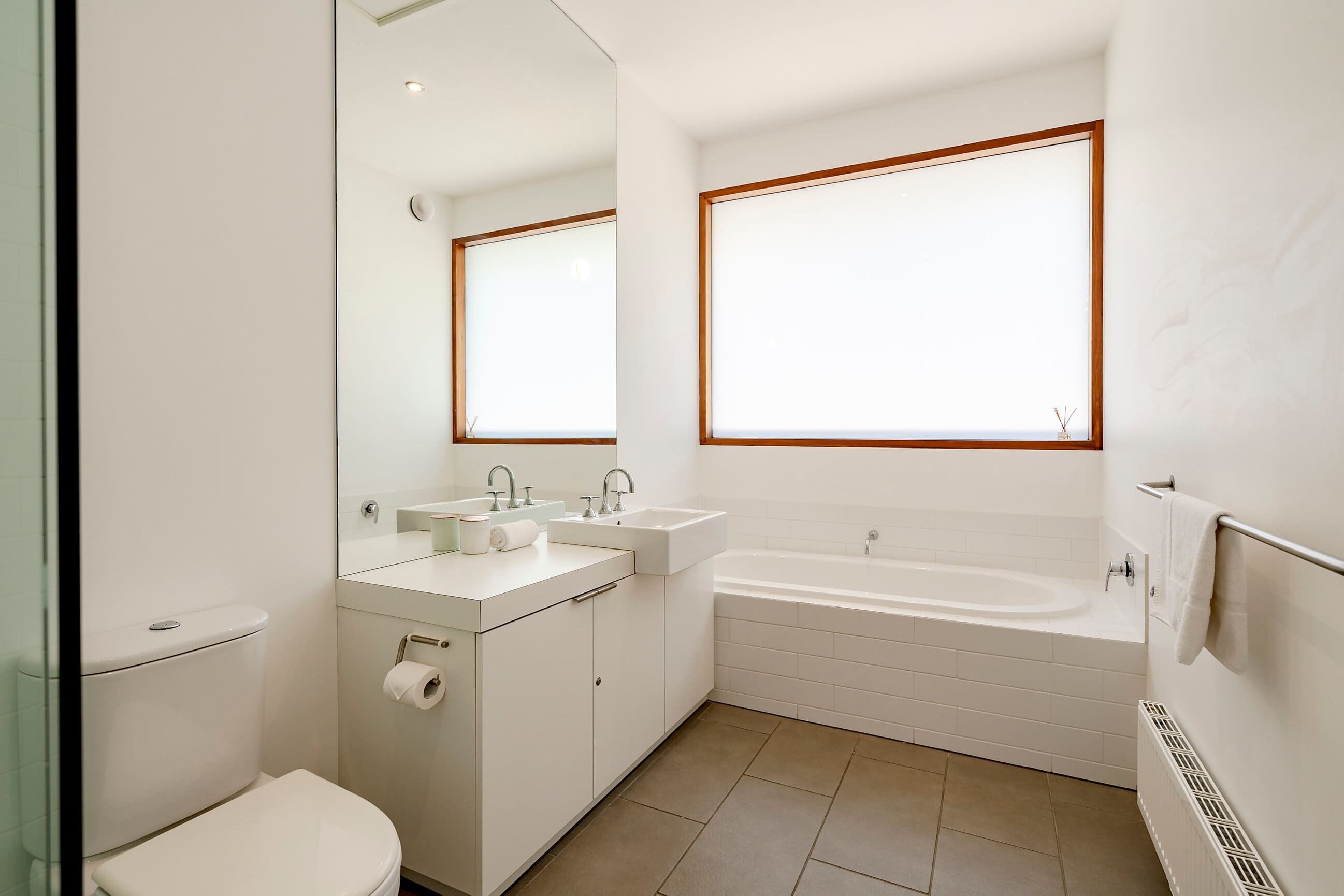 A modern bathroom with a toilet, sink, mirror, and bathtub.