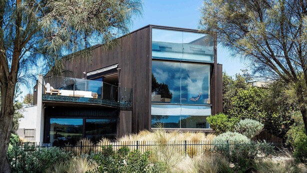 A modern two-story building with large glass windows, a balcony, and a wooden exterior. - Front Row Golf & Lake Views Luxe Coastal Retreat (Torquay)
