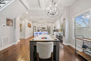 A spacious living area with a pool table, a dining table with chairs, and a chandelier.