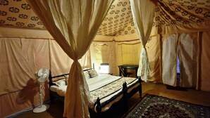 A tent-style room with a bed, a nightstand, a lamp, and a chair. - Prayagraj Cottages By Ganges View Stays (Karchana)