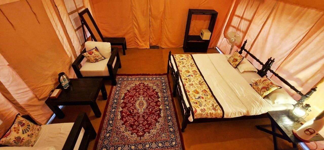 Une pièce aménagée comme une tente, avec un lit, deux chaises, une petite table et un tapis.