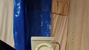 A toilet with a hose attached to the side, positioned on a black platform. - Prayagraj Cottages By Ganges View Stays (Karchana)