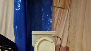 Des toilettes équipées d’un tuyau d’arrosage, installées sur une plateforme noire à l’intérieur d’une structure ressemblant à une tente.