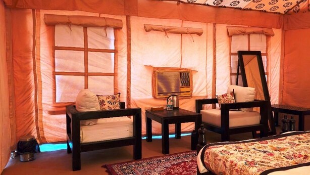 A tent-style room with a bed, two chairs, a small table, and a mirror. - Prayagraj Cottages By Ganges View Stays (Karchana)