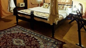 A room with a bed, a bedside table, a lamp, and a patterned rug. - Prayagraj Cottages By Ganges View Stays (Karchana)