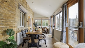 Un espace repas avec un mur en briques, de grandes fenêtres et une table en bois entourée de chaises.