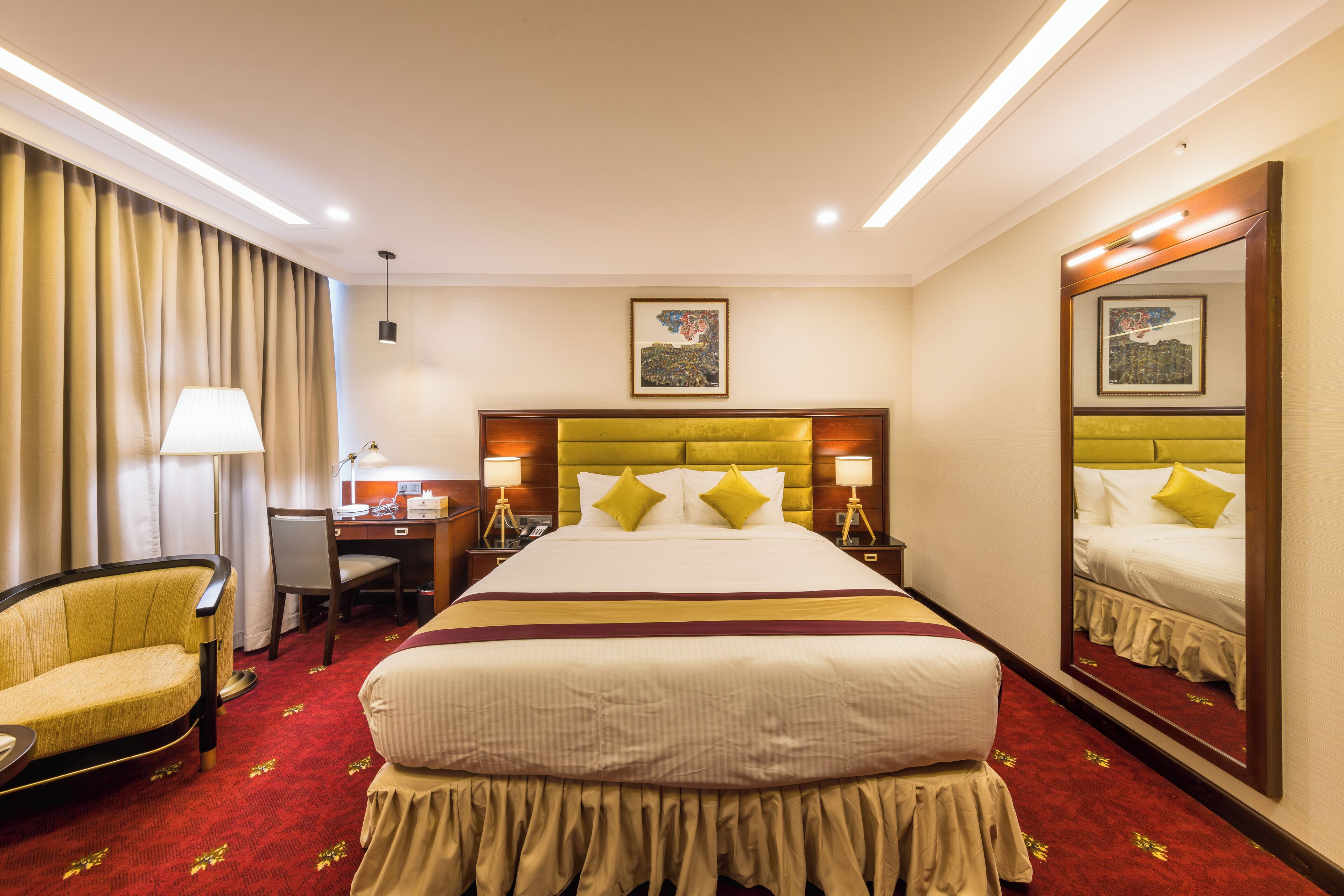 A hotel room with a large bed, a desk, a chair, and a mirror.