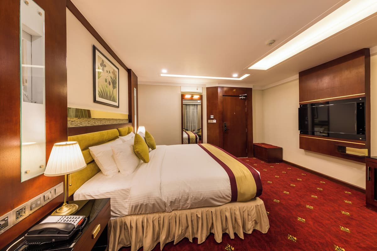 A hotel room with a large bed, a bedside table with a lamp, a telephone, a TV, and a door leading to a bathroom.