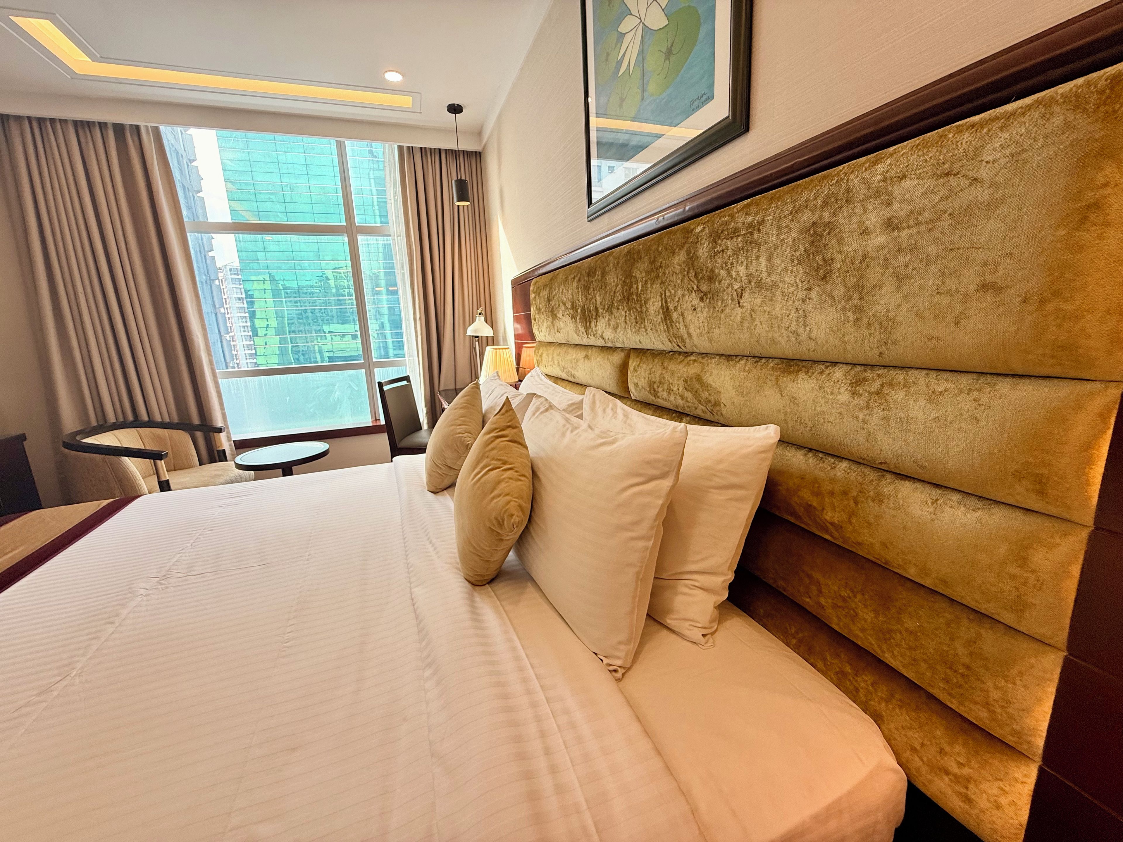 Une chambre d’hôtel avec un grand lit, une tête de lit, une fenêtre avec des rideaux, un bureau et une chaise.