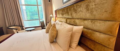 Une chambre d’hôtel avec un grand lit, une tête de lit, une fenêtre avec des rideaux, un bureau et une chaise.