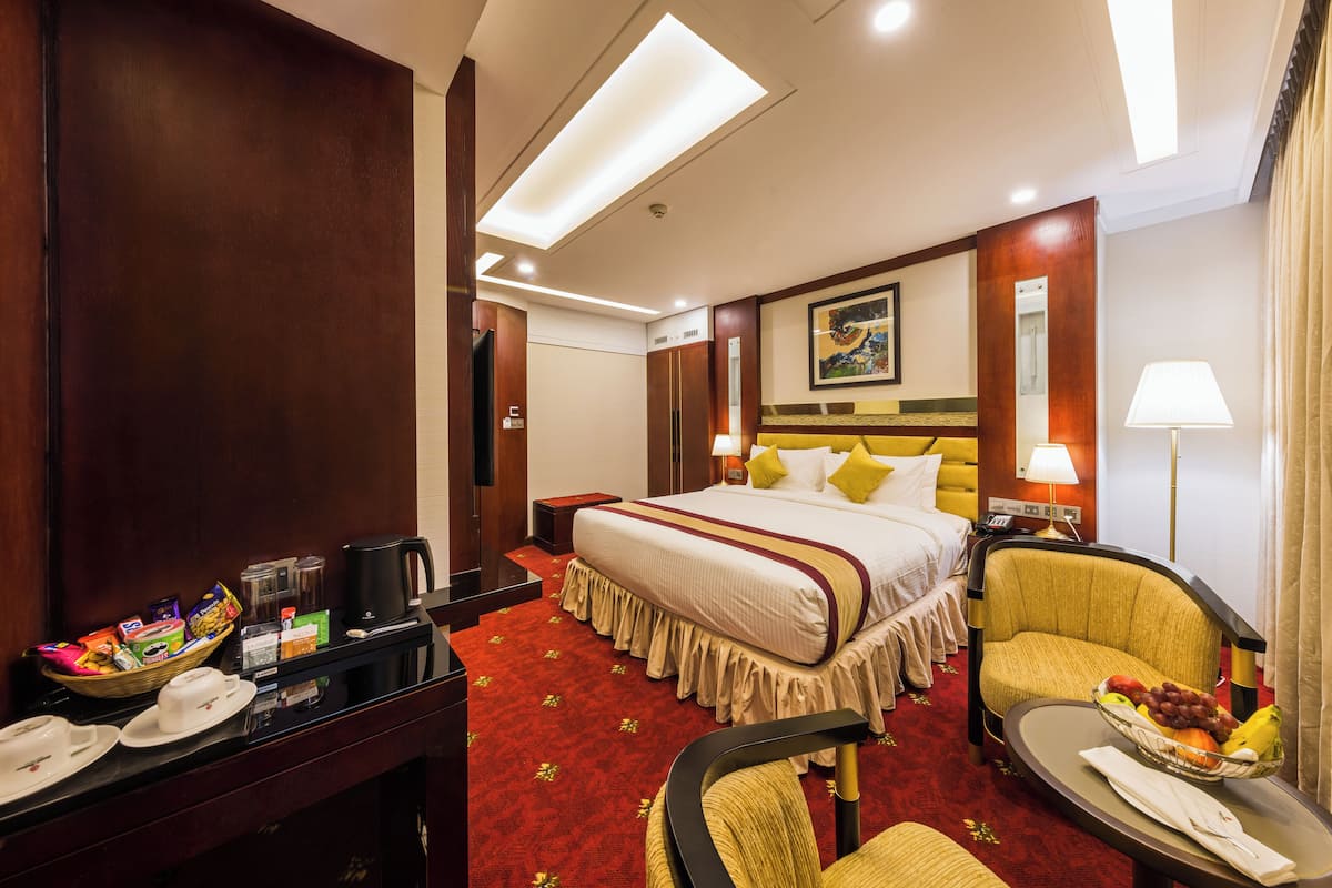 A hotel room with a large bed, a desk with a coffee maker, a chair, and a fruit bowl.