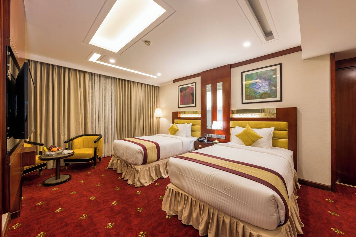 A hotel room with two beds, a TV, a desk with a lamp, and a chair.