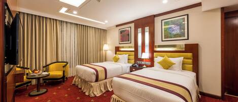 A hotel room with two beds, a TV, a desk with a lamp, and a chair.