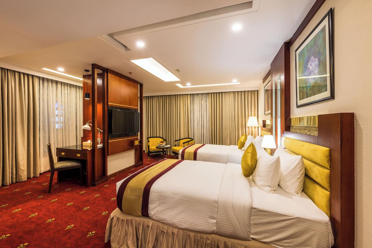 A hotel room with two beds, a desk, a TV, and a chair.