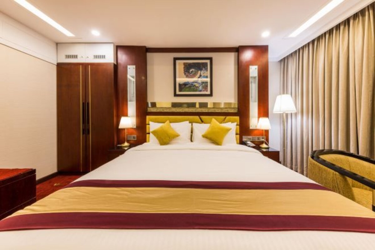 Una habitación de hotel con una cama grande, dos mesitas de noche, un armario y un cuadro en la pared.