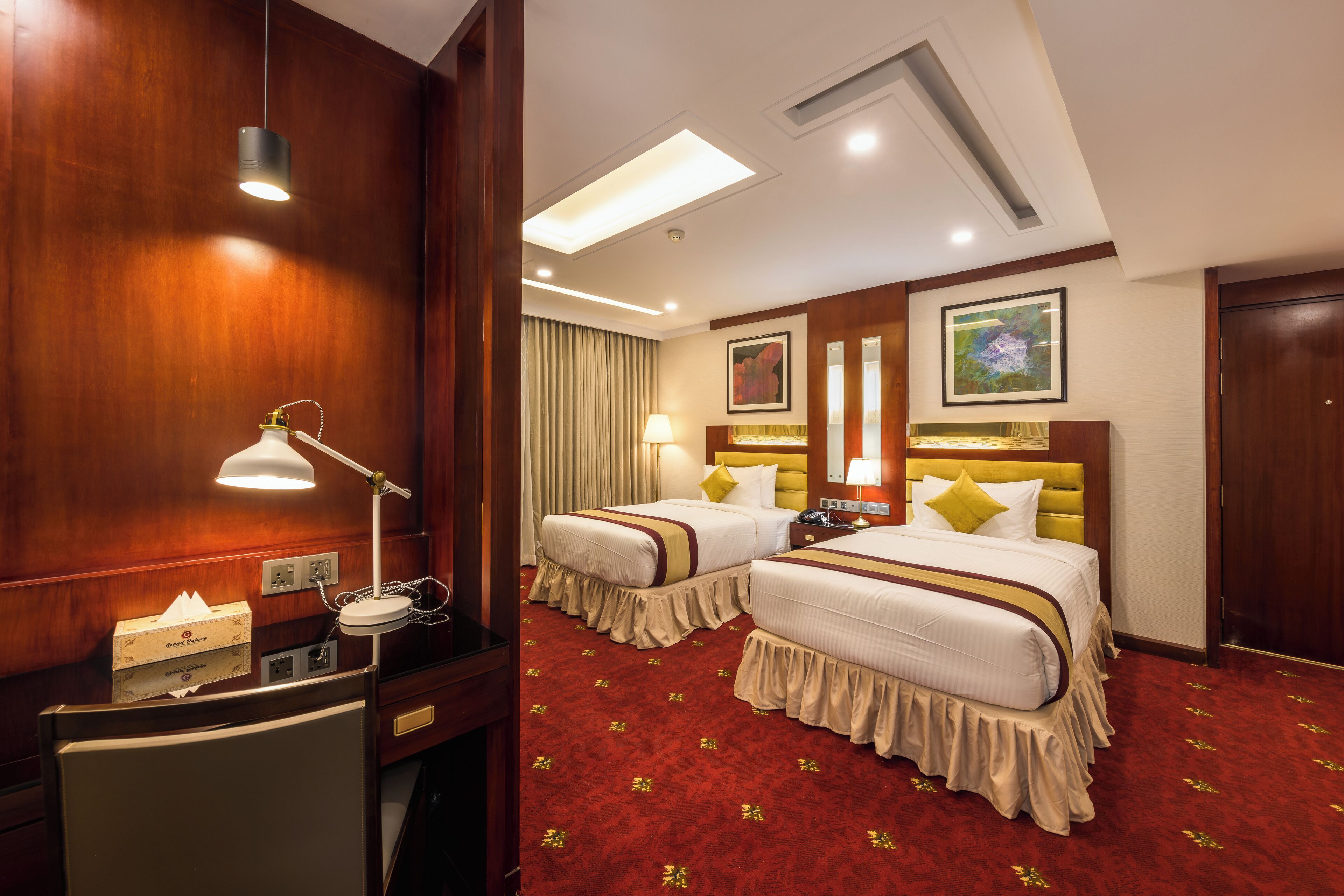 Habitación de hotel con dos camas, un escritorio con lámpara, un minibar y un ventanal con cortinas.