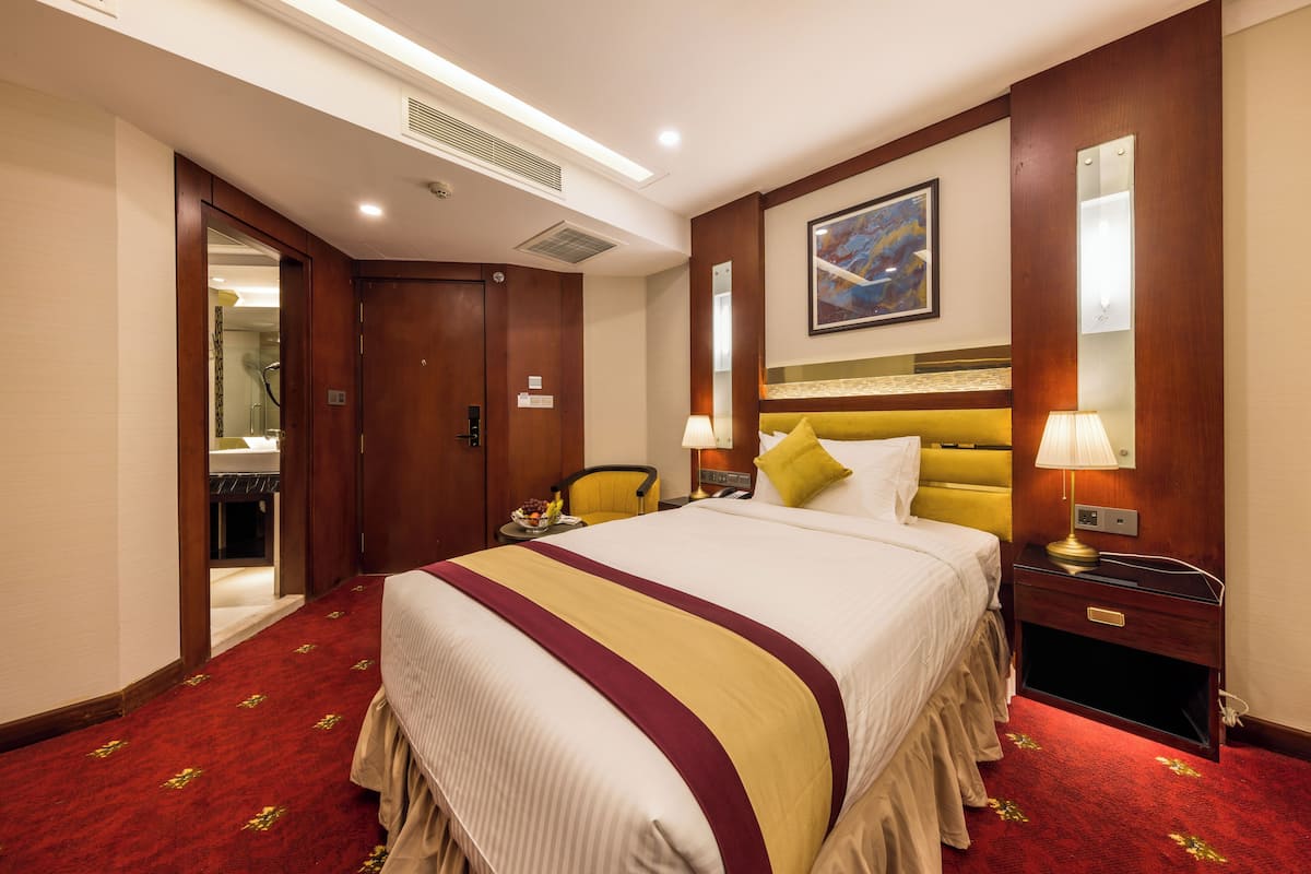 A hotel room with a large bed, a bedside table with a lamp, a mirror, and a painting on the wall.